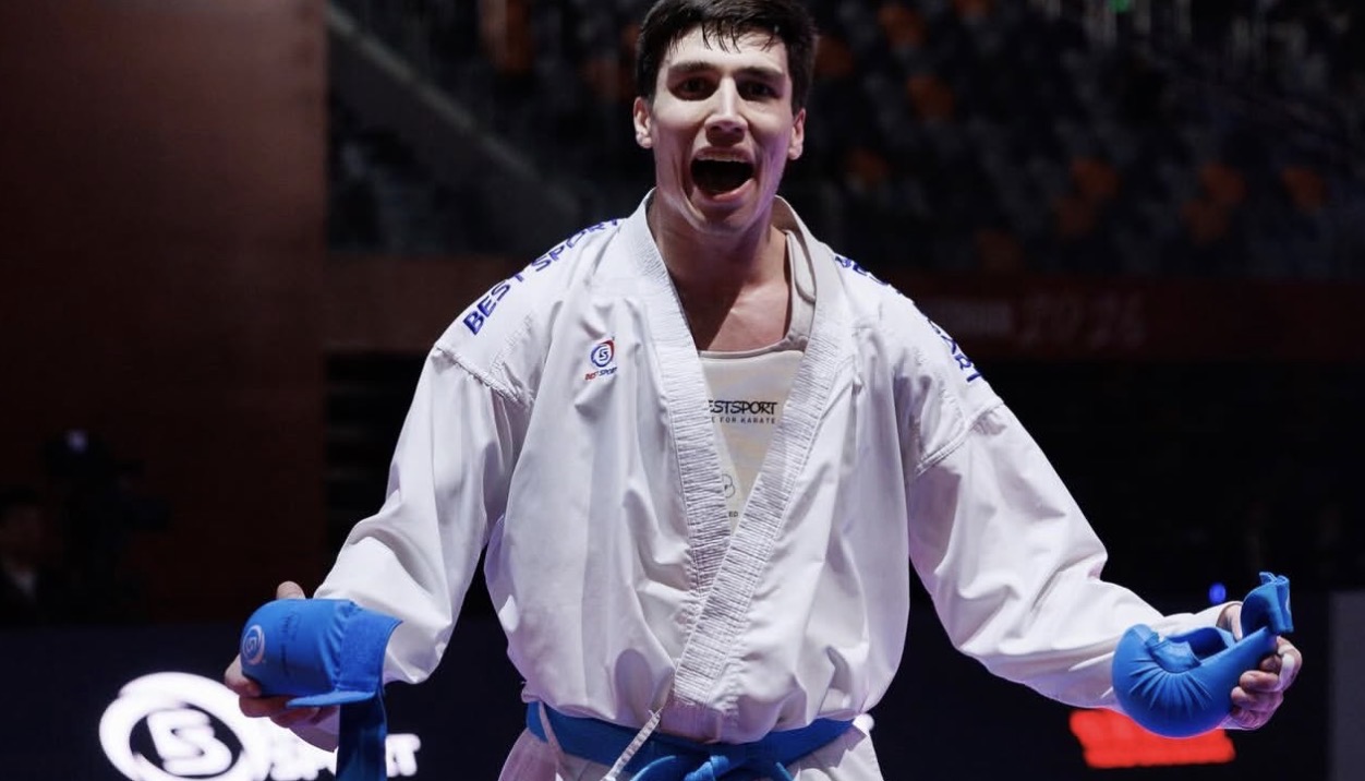 Αθλητής kumite με λευκό Best Sport gi και μπλε γάντια πανηγυρίζει σε αγώνα